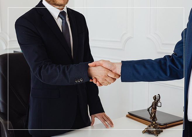 Two men in suits shaking hands over a table.