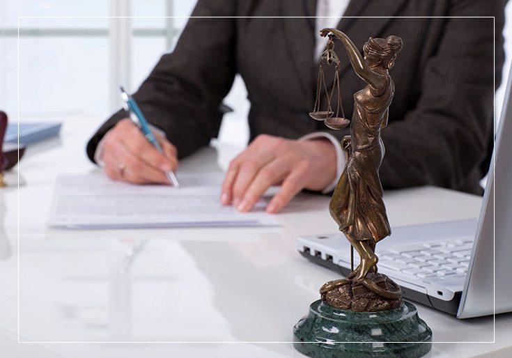 A person writing on paper next to a statue of lady justice.